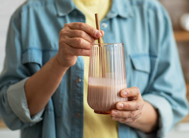 Person Stirring Chocolate Milkshake In A Glass With A Straw